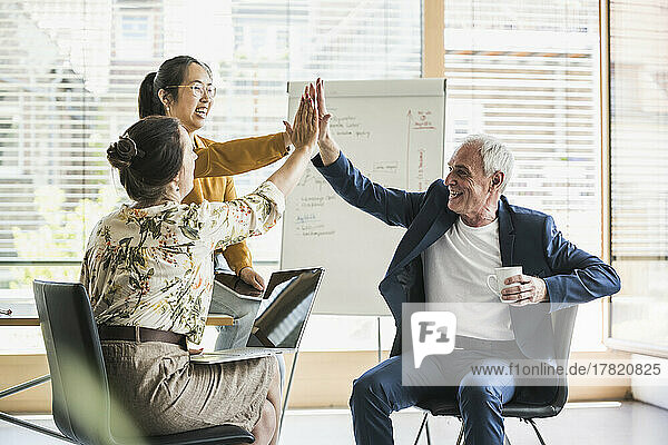 Happy business colleagues giving high-five to each other at work place