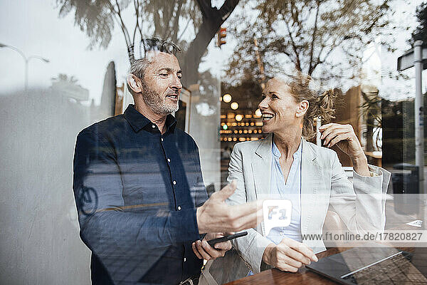Smiling businessman talking with businesswoman in cafe seen through glass