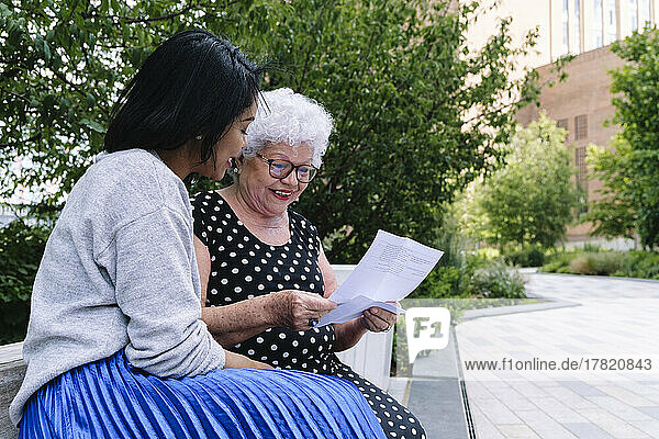 Surprised senior woman reading letter sitting by daughter at park