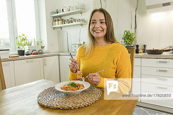 Happy woman eating spaghetti sitting at dinning table at home