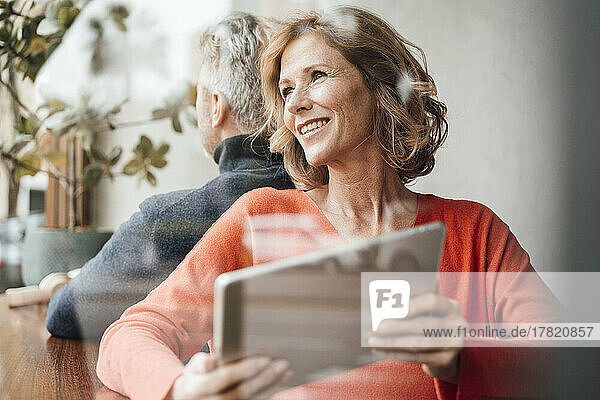 Lächelnde Frau mit Tablet-PC sitzt vor Mann im Café