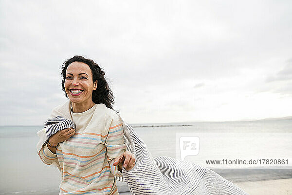 Glückliche Frau mit Schal  die vor dem Meer steht