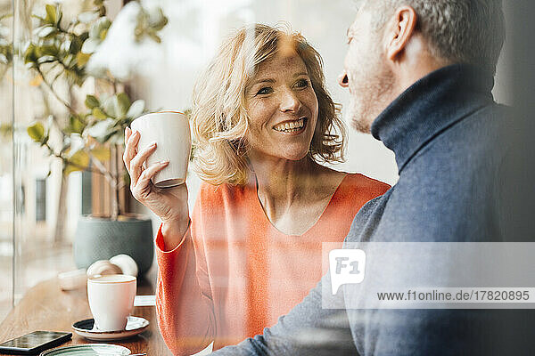 Happy woman holding coffee cup talking with man in cafe