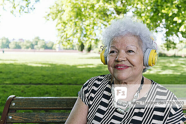 Happy senior woman with wireless headphones listening music at park
