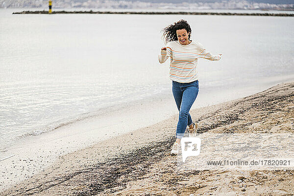 Fröhliche Frau läuft am Strand auf Sand
