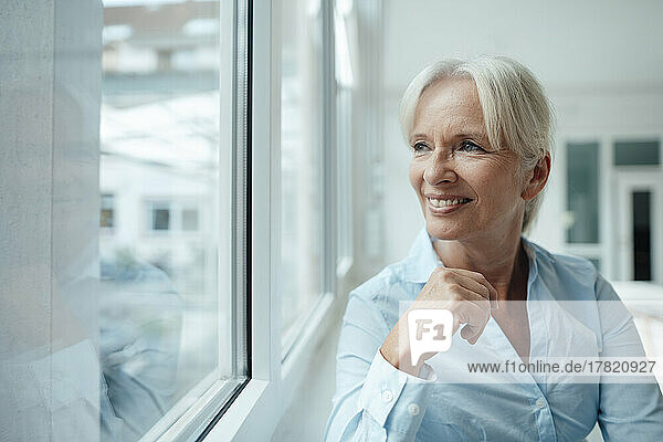 Happy senior businesswoman looking through window in office