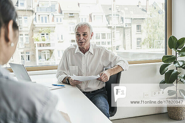 Senior businessman holding document discussing with colleague in office