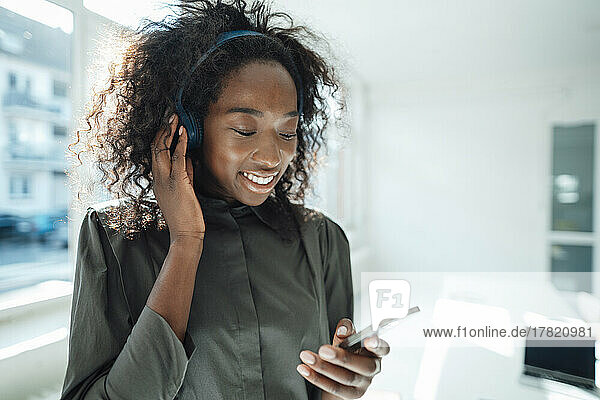 Smiling youngwoman using smart phone listening music through wireless headphones