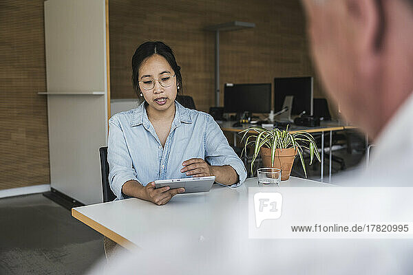 Businesswoman using tablet PC and discussing work with colleague at desk