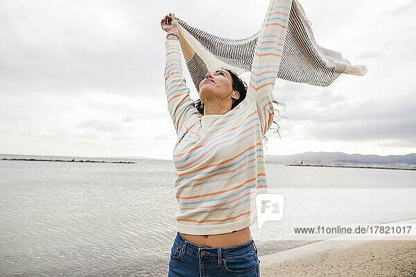 Mature woman holding scarf standing at beach