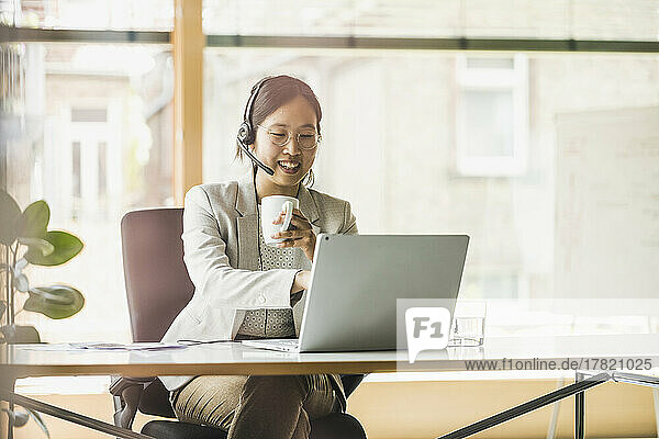 Happy businesswoman wearing headset working on laptop in office