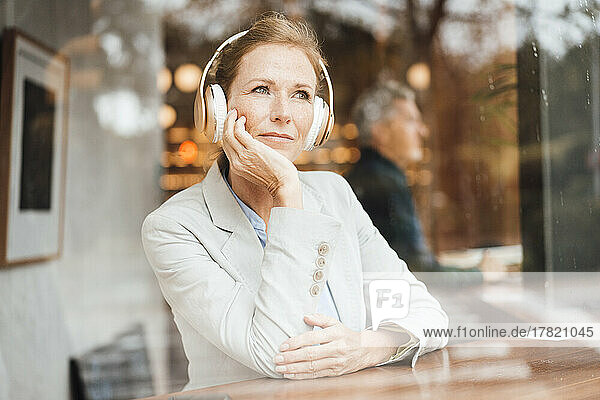 Businesswoman with head in hand listening music through wireless headphones in cafe