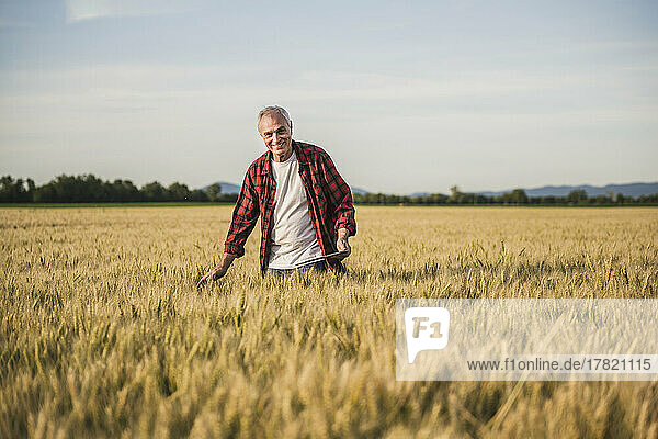 Happy farmer standing amidst wheat crops on field