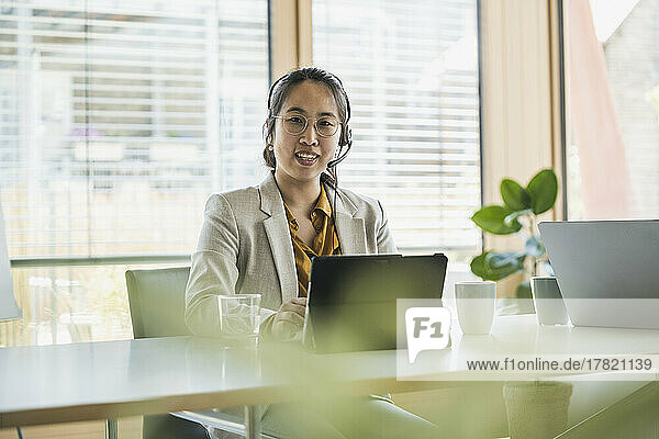 Happy businesswoman wearing headset sitting at desk in office