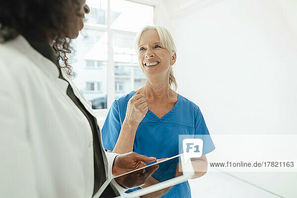 Lächelnde Krankenschwester im Gespräch mit einer Ärztin  die einen Tablet-PC hält