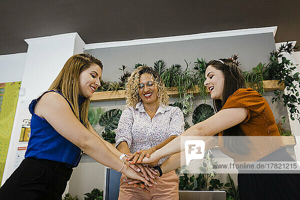 Happy businesswomen stacking hands together in office