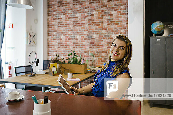 Glückliche Geschäftsfrau sitzt mit Tablet-PC am Schreibtisch im Büro