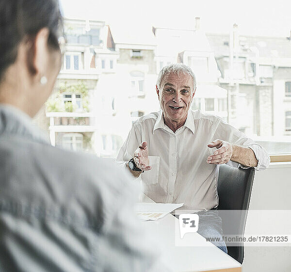 Glücklicher älterer Geschäftsmann  der mit einem Kollegen im Büro diskutiert