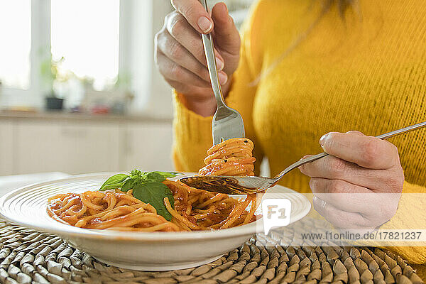 Hands of woman holding fork with spaghetti at home