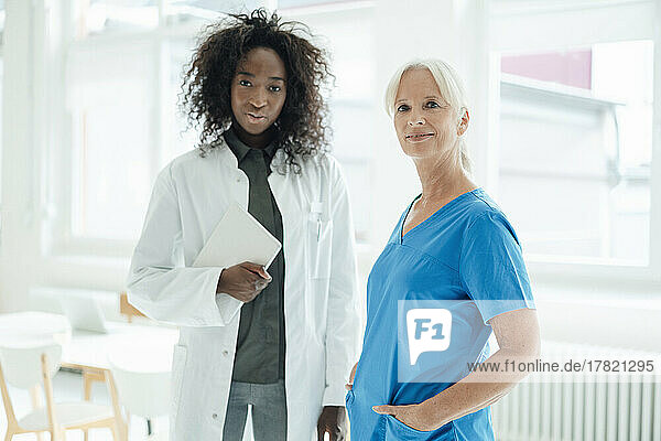 Nurse with hands in pockets standing by female doctor holding tablet PC