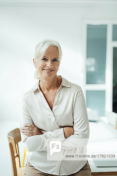 Smiling senior businesswoman with arms crossed in office