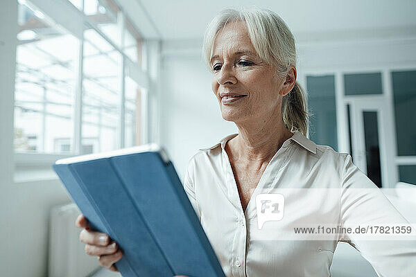 Smiling senior businesswoman holding tablet PC in office