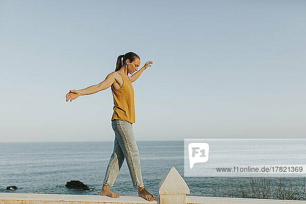 Woman balancing on railing at the sea on sunny day