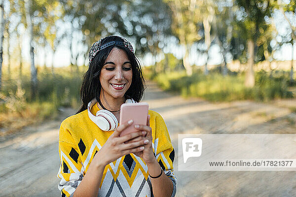 Smiling woman with wireless headphones using smart phone in nature