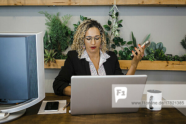 Businesswoman with mobile phone using laptop at desk in office