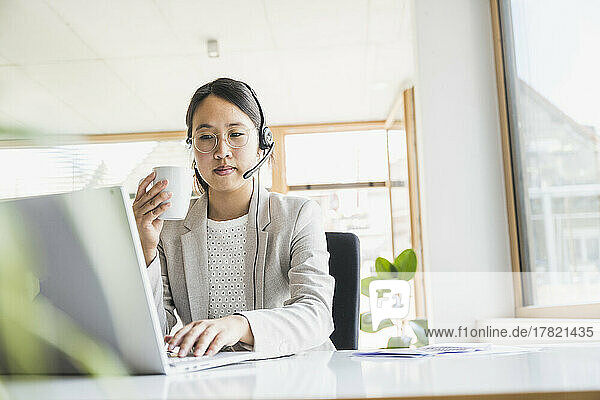 Businesswoman with coffee cup working on laptop at desk