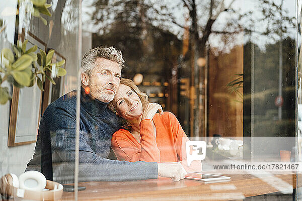 Smiling woman with man sitting in cafe seen through glass