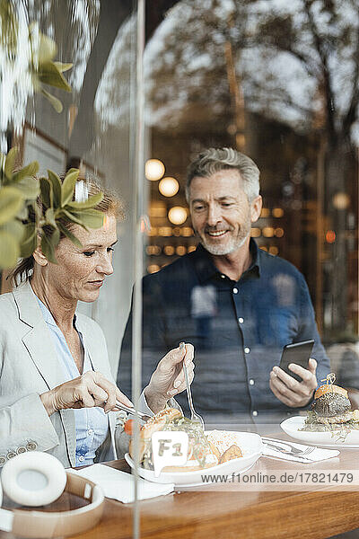 Geschäftsfrau mit Geschäftsmann hält Mobiltelefon beim Mittagessen im Café