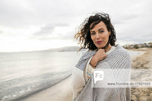 Smiling woman wrapped in scarf at beach