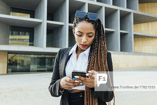 Young businesswoman with mobile phone standing outside office building