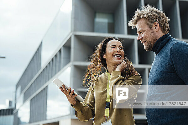 Happy businesswoman holding tablet PC talking with colleague