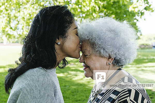 Tochter küsst Mutter im Park auf die Stirn