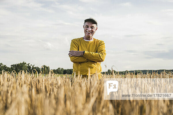 Happy farmer with arms crossed standing in wheat farm