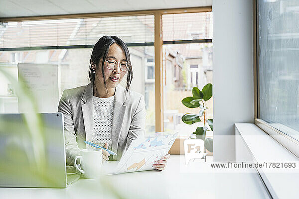 Geschäftsfrau mit Brille liest Dokument im Büro