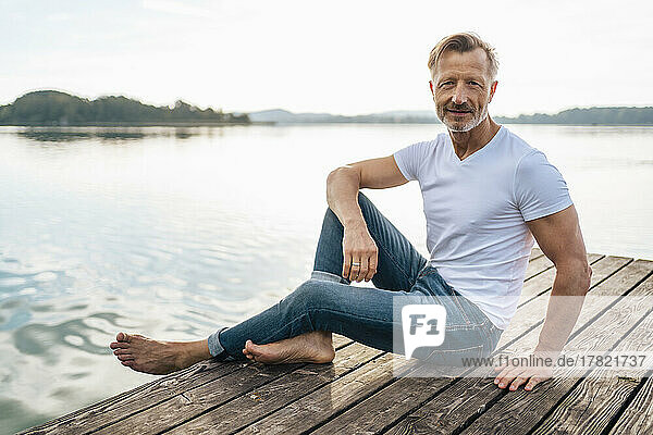Smiling mature man sitting on jetty at lake