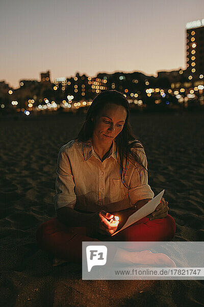 Woman burning paper with cigarette lighter sitting on beach at night