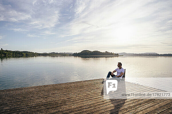 Mature man sitting on pier by lake