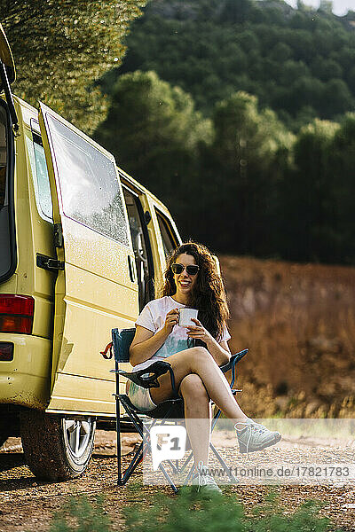 Woman with coffee cup sitting by van