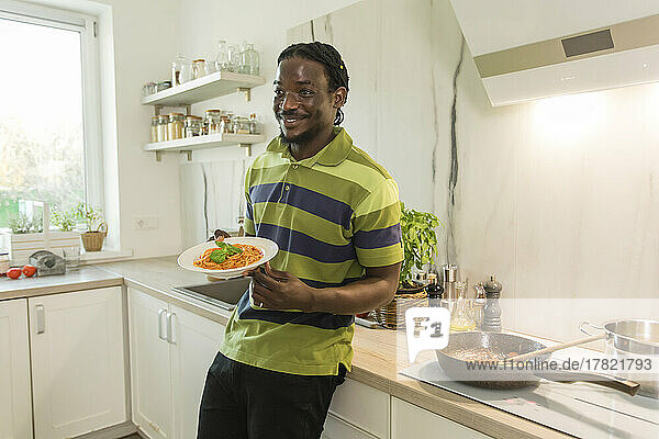 Lächelnder Mann hält einen Teller Spaghetti in der Küche
