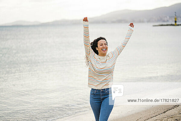 Glückliche Frau mit erhobenen Armen  die am Strand spaziert