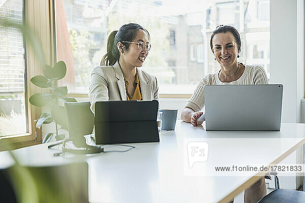Happy mature businesswoman with colleague discussing over laptop in office