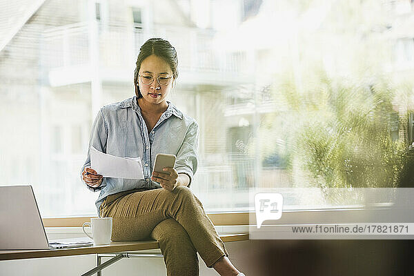 Businesswoman with document and smart phone at office