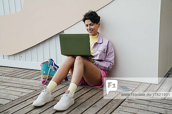 Happy woman using laptop sitting in front of wall