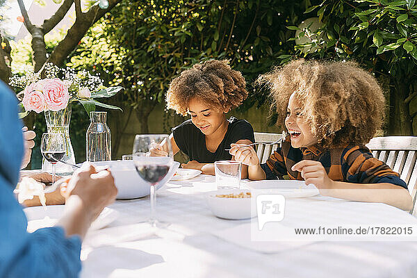 Happy boy with sister eating lunch at dining table in backyard