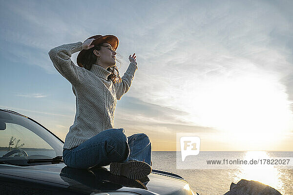 Young woman wearing hat sitting on car hood