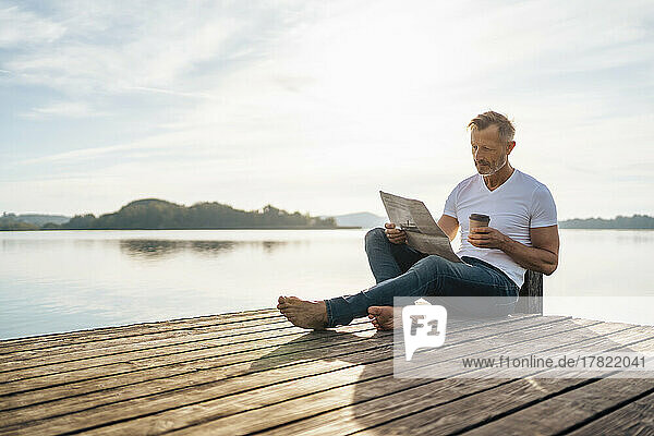 Reifer Mann liest Zeitung und trinkt Kaffee am Pier am See